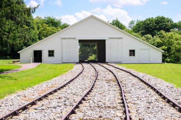 A white barn-like building in Blair County with a railway track leading into its open doors, surrounded by green grass and trees.