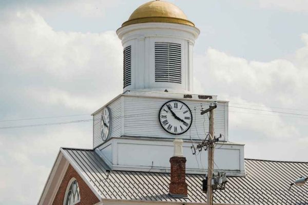 The Bedford County Courthouse in Pennsylvania stands with a golden-domed clock tower and an American flag waving on top, set against a cloudy sky.